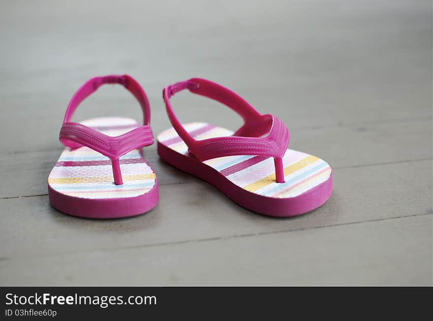 A little girl's thong sandals sit on a wooden floor. A little girl's thong sandals sit on a wooden floor.