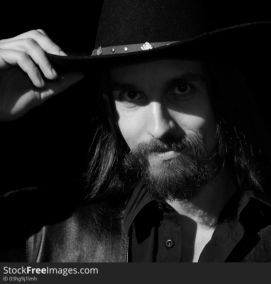 Man with beard and long hair touching his hat, black and white. Man with beard and long hair touching his hat, black and white