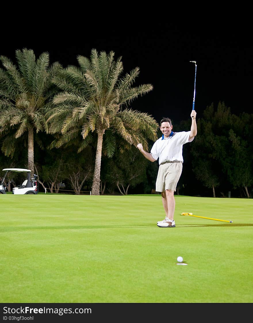 A male golfer celebrates an imminently successful putt during a night game. A male golfer celebrates an imminently successful putt during a night game.