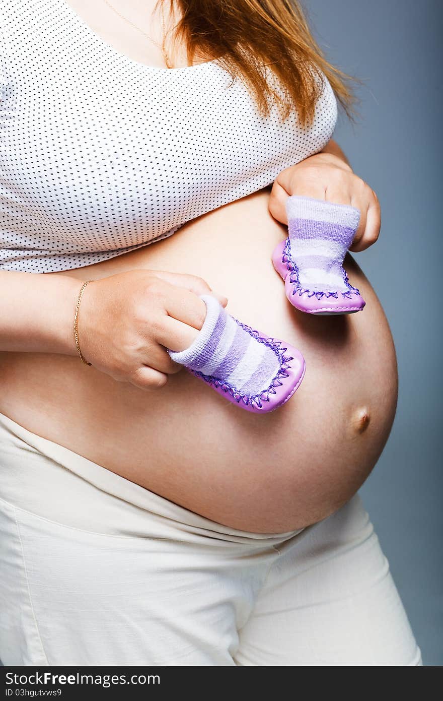 Pregnant woman holding pair of shoes for baby