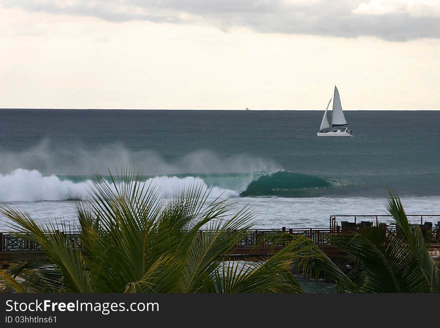 Beach scene with crashing waves and lonely sailboat in Mauritius. Beach scene with crashing waves and lonely sailboat in Mauritius.