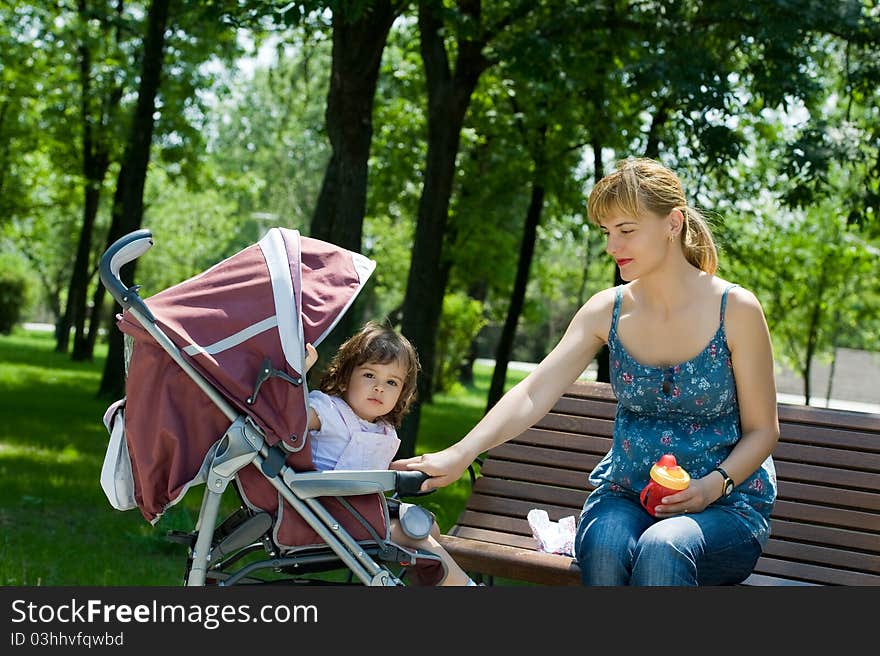 Young woman on bench with a pram in a park