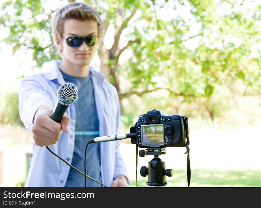 Young man holding a microphone connected to a D SLR. Focus on the microphone only. Young man holding a microphone connected to a D SLR. Focus on the microphone only.