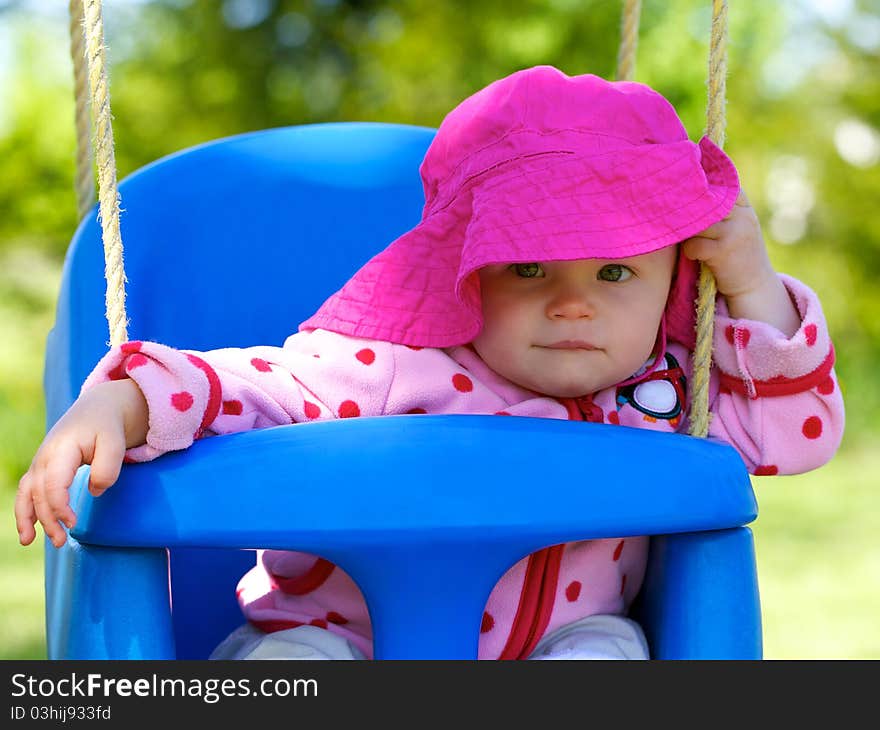 Infant’s sitting happily in swing with floppy bright colored sun hat. Infant’s sitting happily in swing with floppy bright colored sun hat