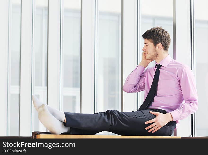 Young business man talk by cellphone over bright window in big hall