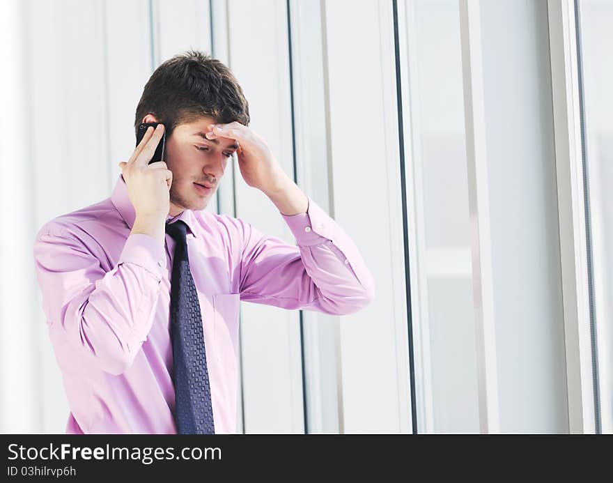 Young business man talk by cellphone over bright window in big hall