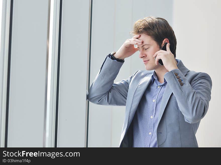 Young business man talk by cellphone over bright window in big hall