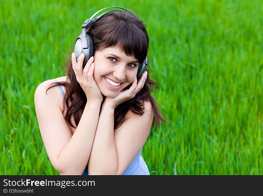 Happy smiley girl with the headphones on a grass