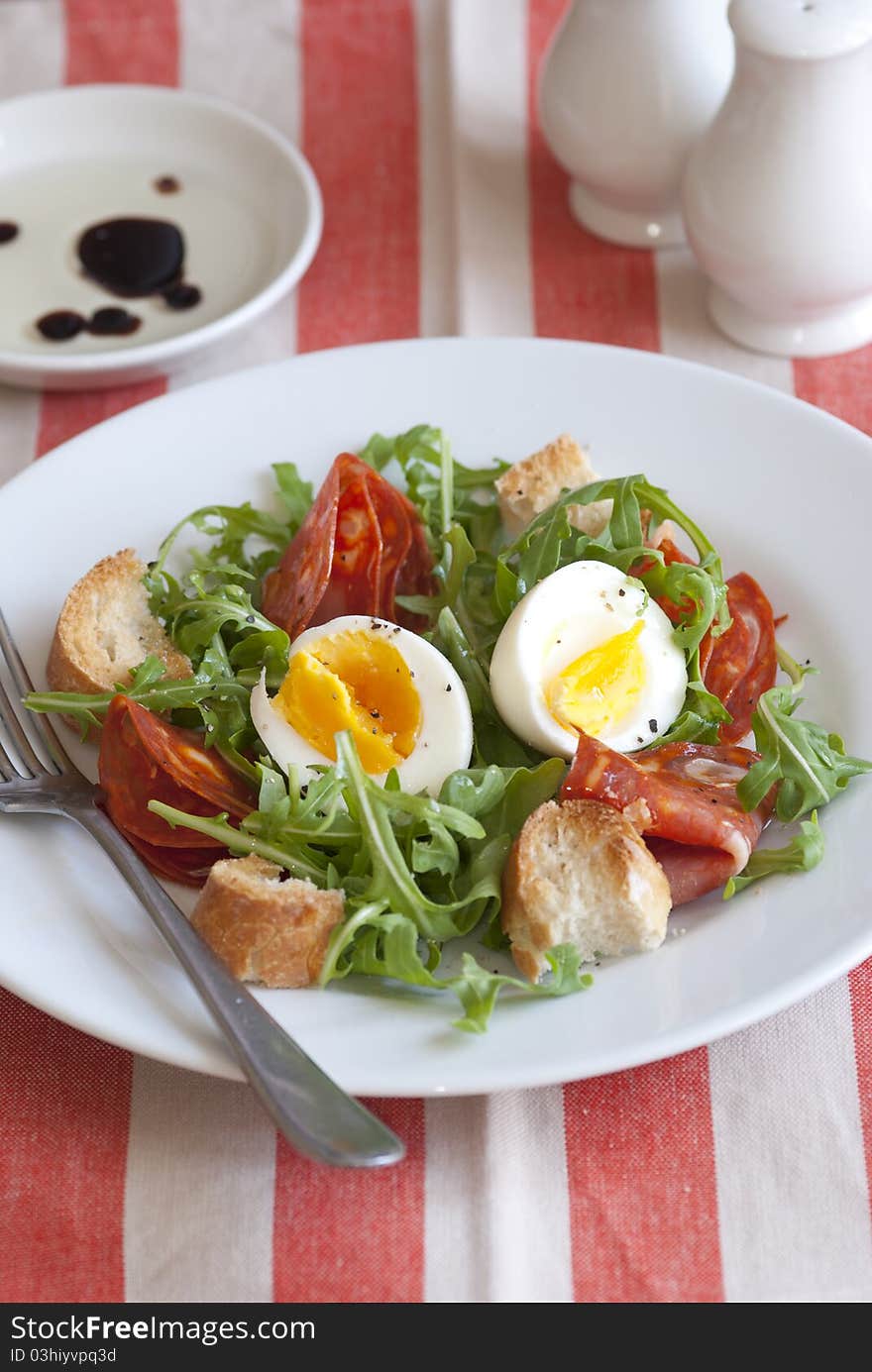 Soft-boiled egg, chorizo and rocket salad on a plate. Soft-boiled egg, chorizo and rocket salad on a plate