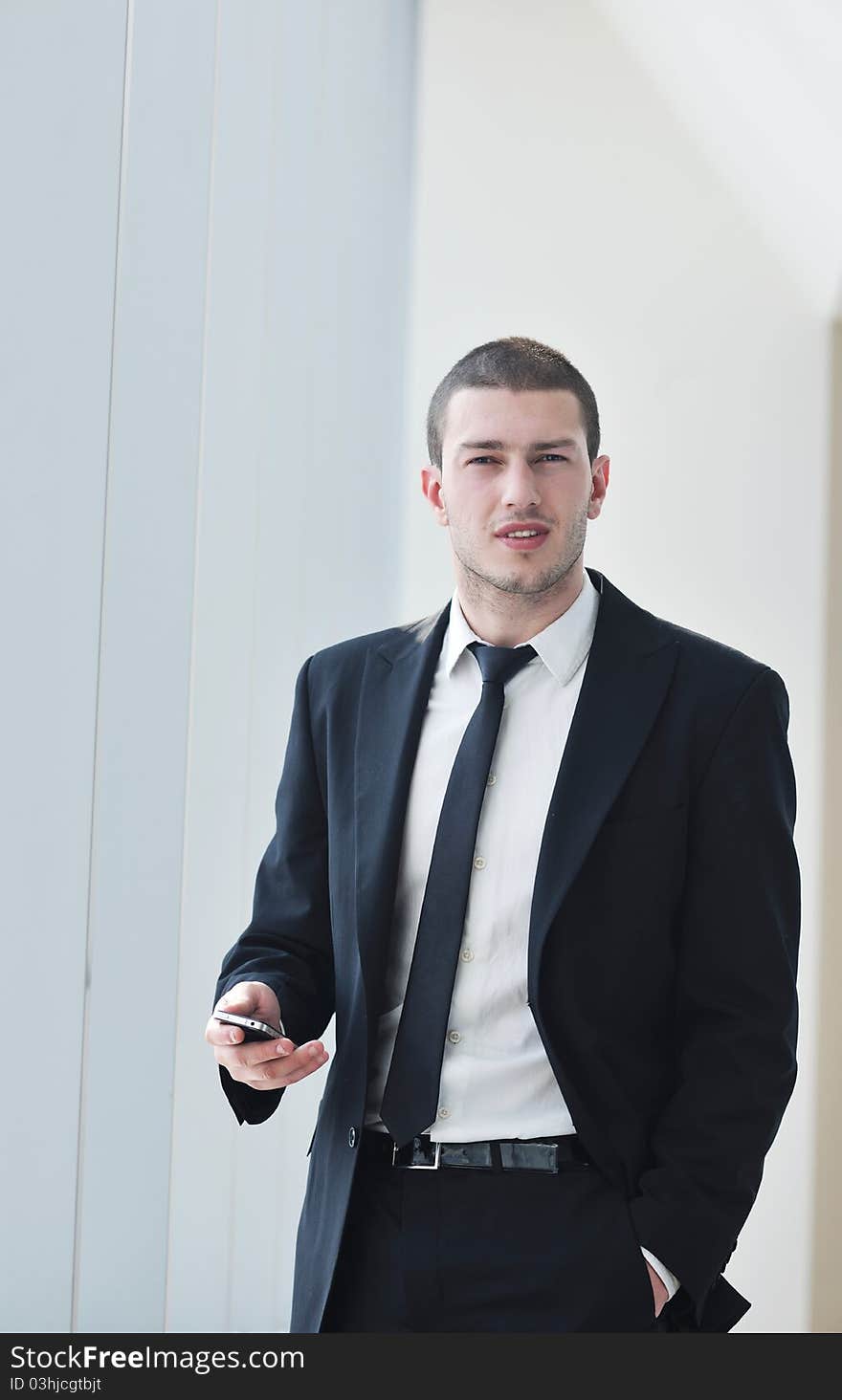 Young business man talk by cellphone over bright window in big hall