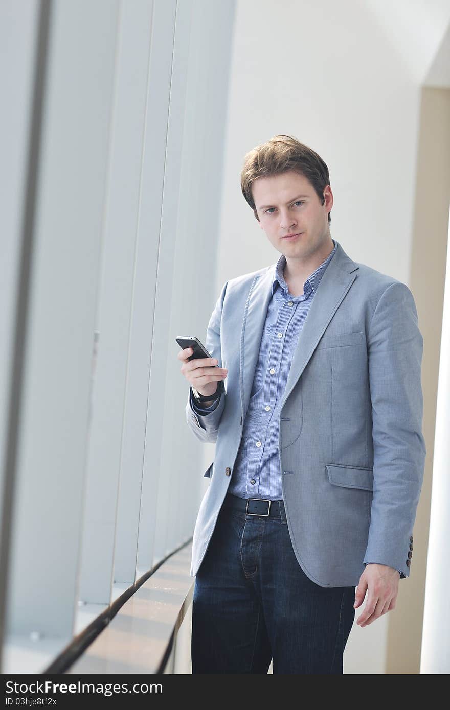 Young business man talk by cellphone over bright window in big hall