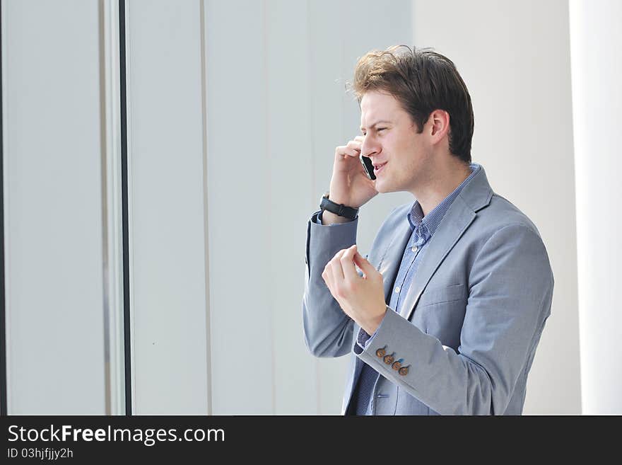 Young business man talk by cellphone over bright window in big hall