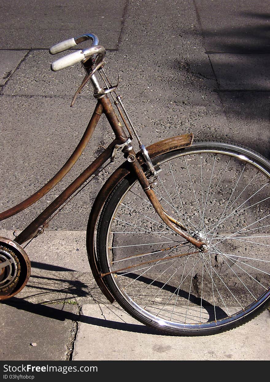 Half of an old rusty utility bicycle with a neutral concrete background. Half of an old rusty utility bicycle with a neutral concrete background