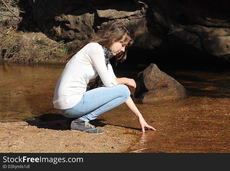 Young woman gently dipping her hand into the cold shallow water. Young woman gently dipping her hand into the cold shallow water