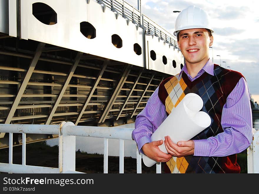 Industrial theme: architect, on a workplace, in a warm winter jacket and a helmet, has control over a tablet. Industrial theme: architect, on a workplace, in a warm winter jacket and a helmet, has control over a tablet.