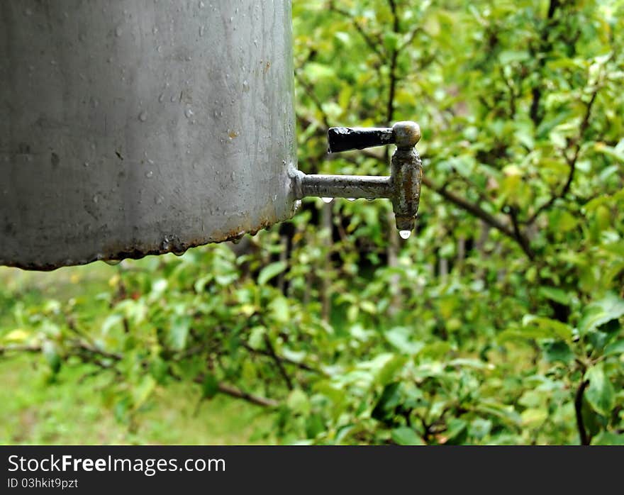 Water tap with drops on rustic metallic container outdoors