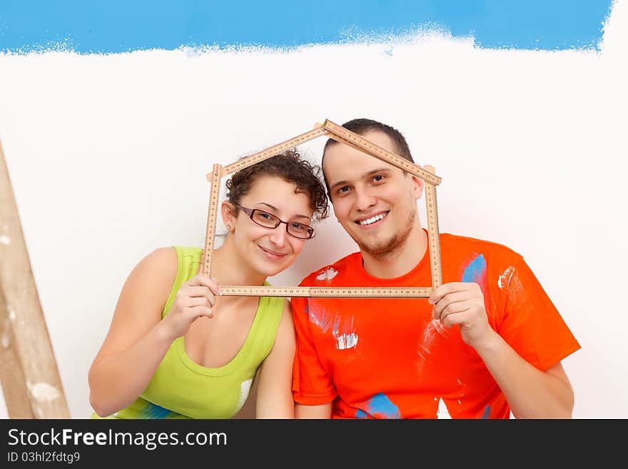 Happy couple with a folding rule in their hands in form of a house. Happy couple with a folding rule in their hands in form of a house