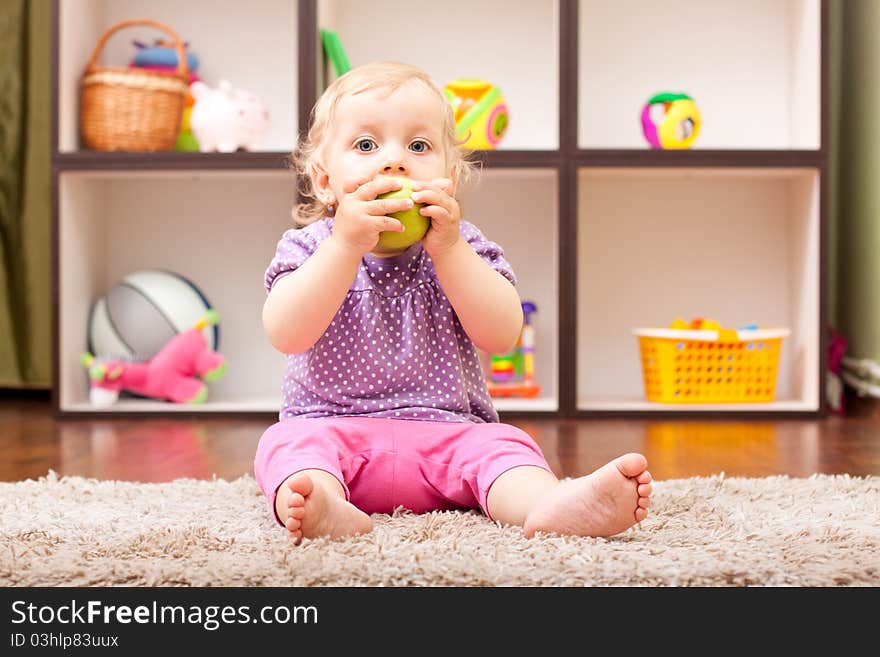 Cute baby girl eating a green apple in her room. Cute baby girl eating a green apple in her room