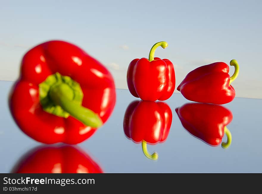 Three red peppers on mirror and sky background