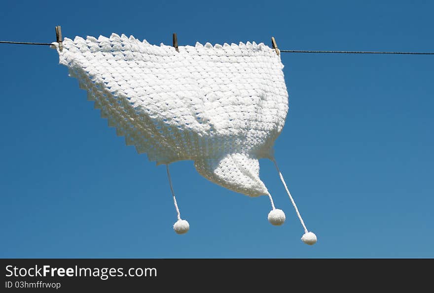 A hand knitted baby shawl hangs drying on a clothesline against a brilliant blue sky with copy space. A hand knitted baby shawl hangs drying on a clothesline against a brilliant blue sky with copy space.