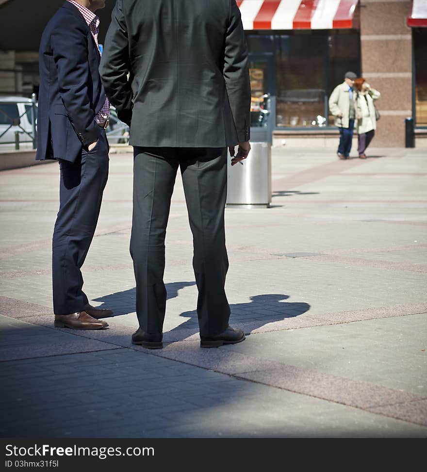 Businessmen standing with cigarette. Elderly couple on the background.