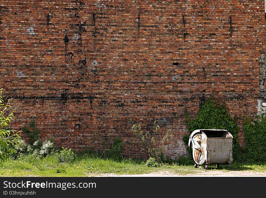 Garbage can by the red brick wall.