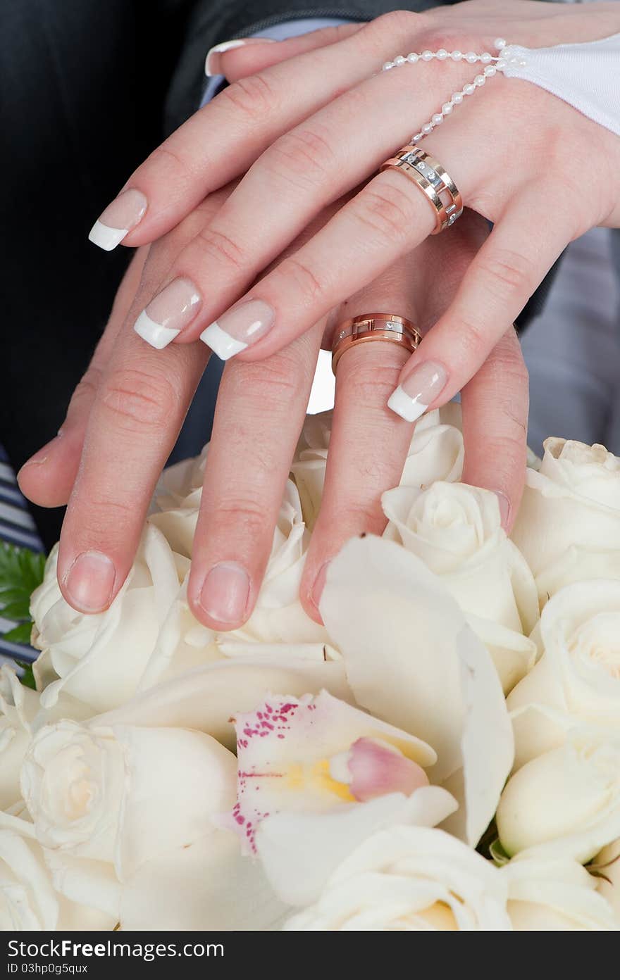 Photo of two tender hands of the groom and the bride with wedding rings and bouquet of white roses close up. Photo of two tender hands of the groom and the bride with wedding rings and bouquet of white roses close up