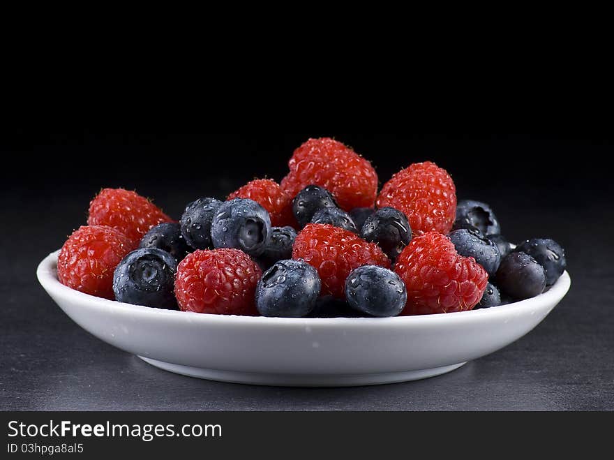 Plate of fresh blueberries and raspberries on black background