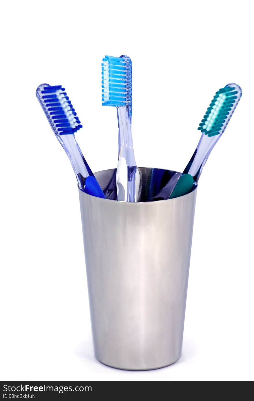 Three toothbrushes in a metal cup on white background