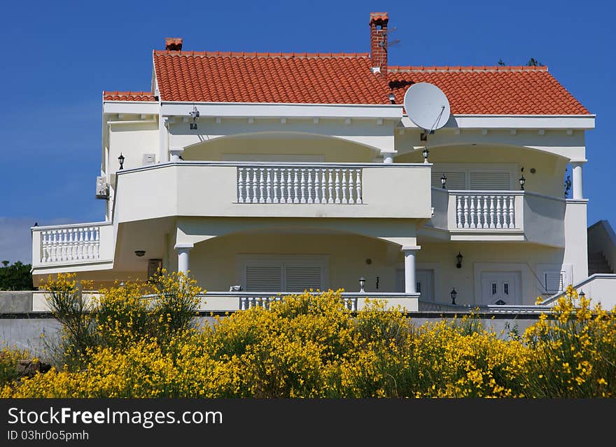 White villa is decorated with yellow flowers in front of it. In the background is blue blue sky. White villa is decorated with yellow flowers in front of it. In the background is blue blue sky.