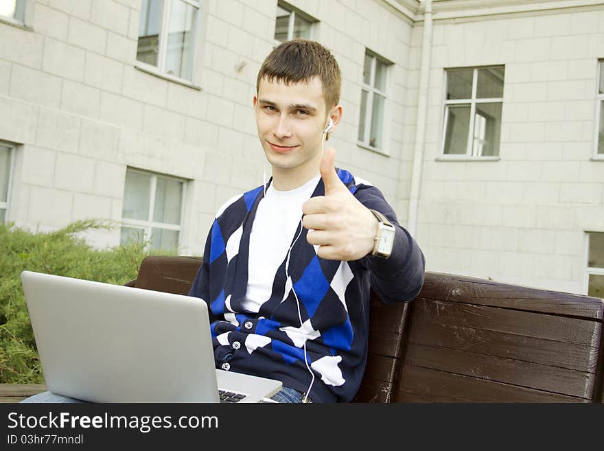 Close-up of a young male student with a laptop on campus. Thumbs up. Close-up of a young male student with a laptop on campus. Thumbs up