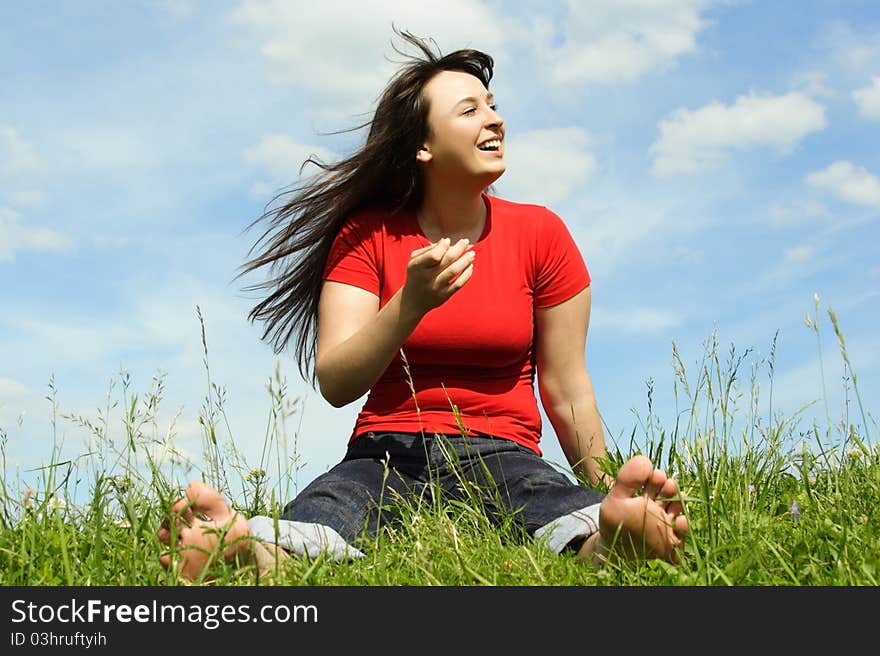 Young barefooted women siting on summer meadow and smiling, blue sky