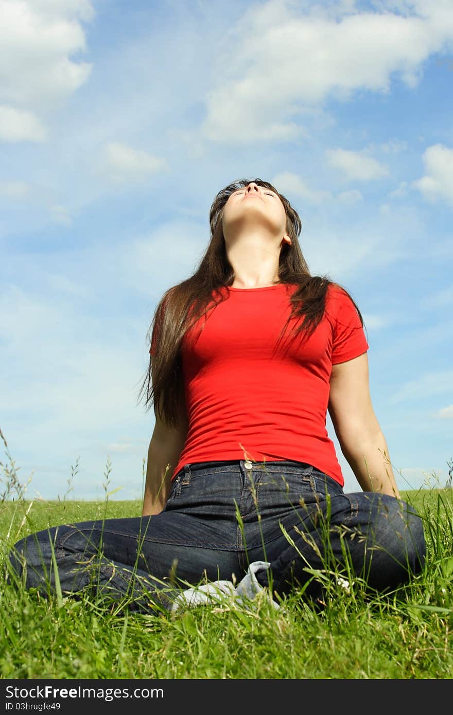 Young girl siting on summer meadow and looking up, blue sky