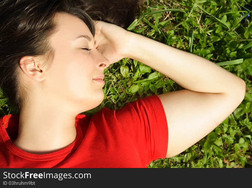 Closeup of young brunette girl lying on summer meadow and smiling, closed eyes