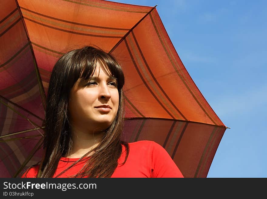 Young brunette girl holding red umbrella, blue sky