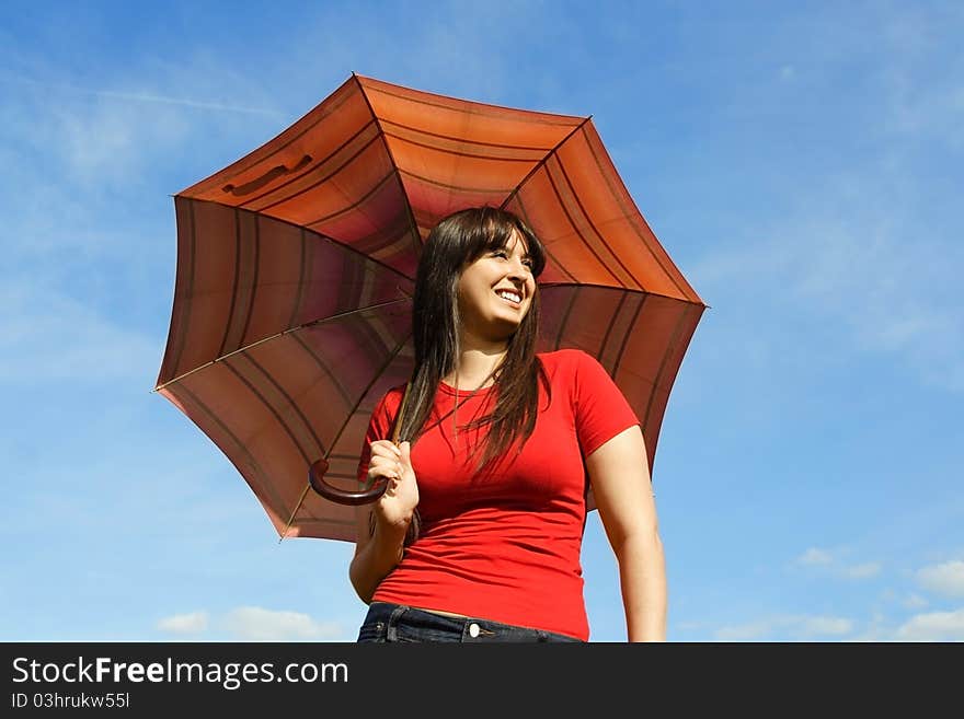 Young brunette girl in red shirt holding red umbrella and smiling, blue sky. Young brunette girl in red shirt holding red umbrella and smiling, blue sky