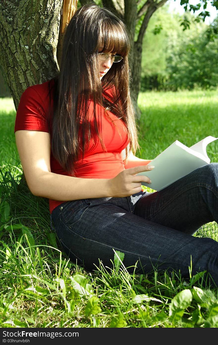 Girl sitting near tree and reading book