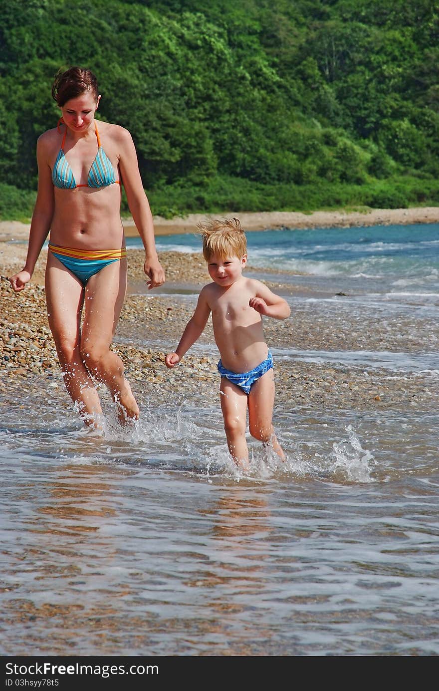 Happy family of mother with kid running on the sea beach