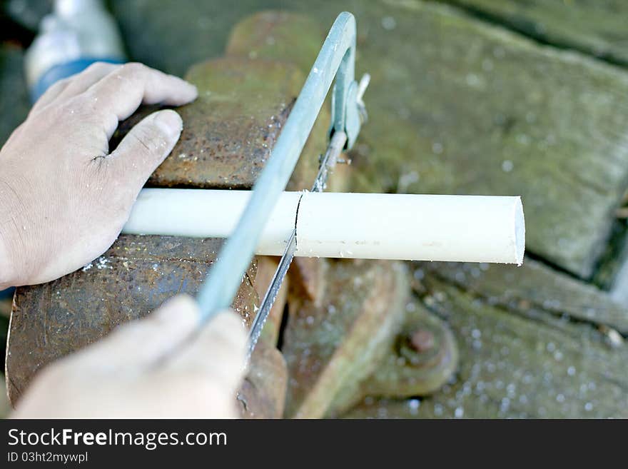 Man saws pipe by handsaw