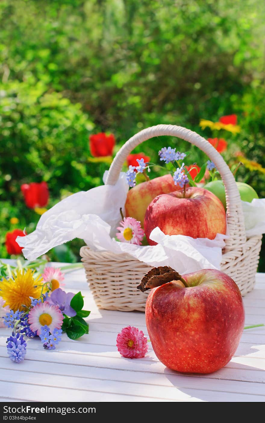 Red apples, flowers and basket on white garden table in sunny summer day. Red apples, flowers and basket on white garden table in sunny summer day