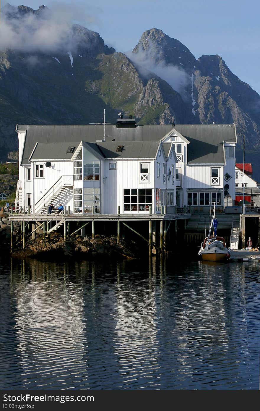 Wooden hotel standing on pillars over the sea with high mountains in the background in Lofoten. Wooden hotel standing on pillars over the sea with high mountains in the background in Lofoten