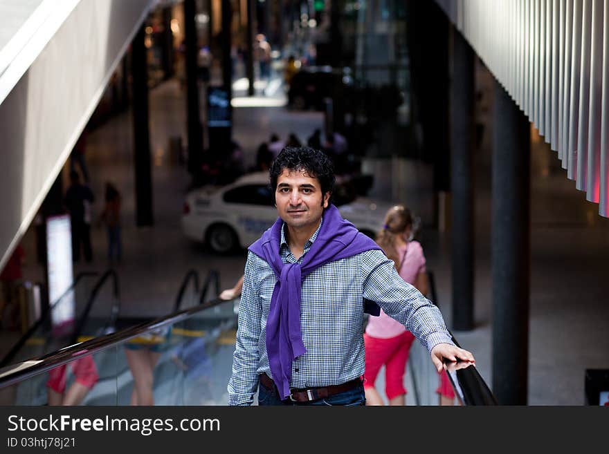 Man in a shopping ceter standing on escalator with 2 blonds behind. Man in a shopping ceter standing on escalator with 2 blonds behind