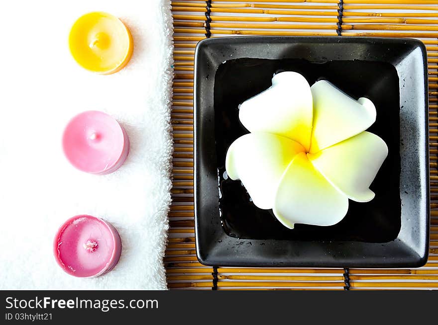 Three candles on white towel with plumeria in the plate on bamboo mat