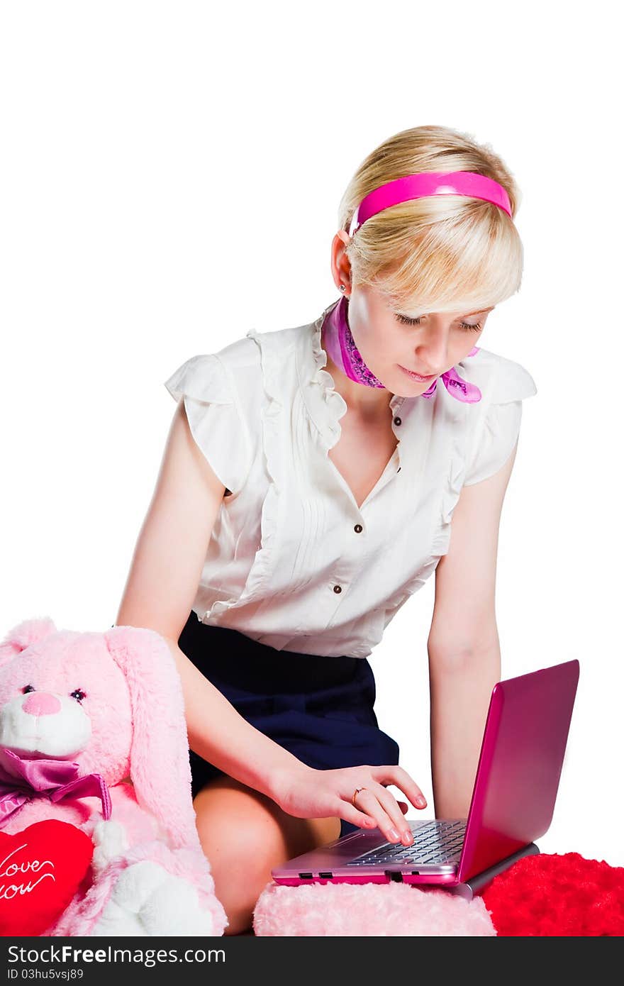 Portrait of beautiful blond girl wearing short skirt and white shoes near pink rabbit working with pink laptop on isolated white background. Portrait of beautiful blond girl wearing short skirt and white shoes near pink rabbit working with pink laptop on isolated white background