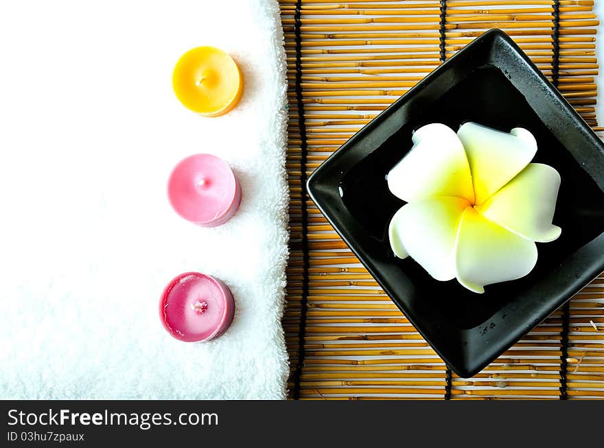 A plumeria in the plate and three candles with white towel on bamboo mat.