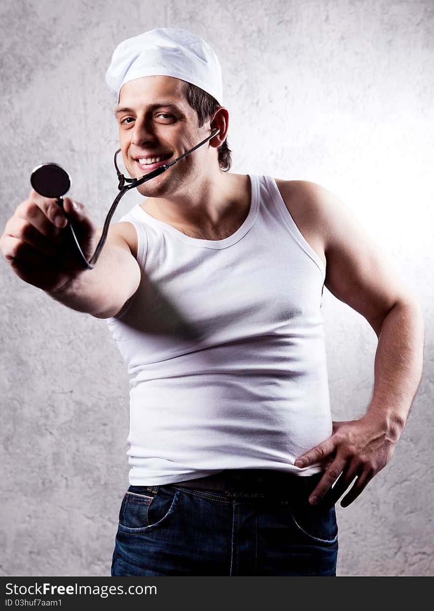 Humorous portrait of a young muscular doctor with a stethoscope, against the old wall. Humorous portrait of a young muscular doctor with a stethoscope, against the old wall