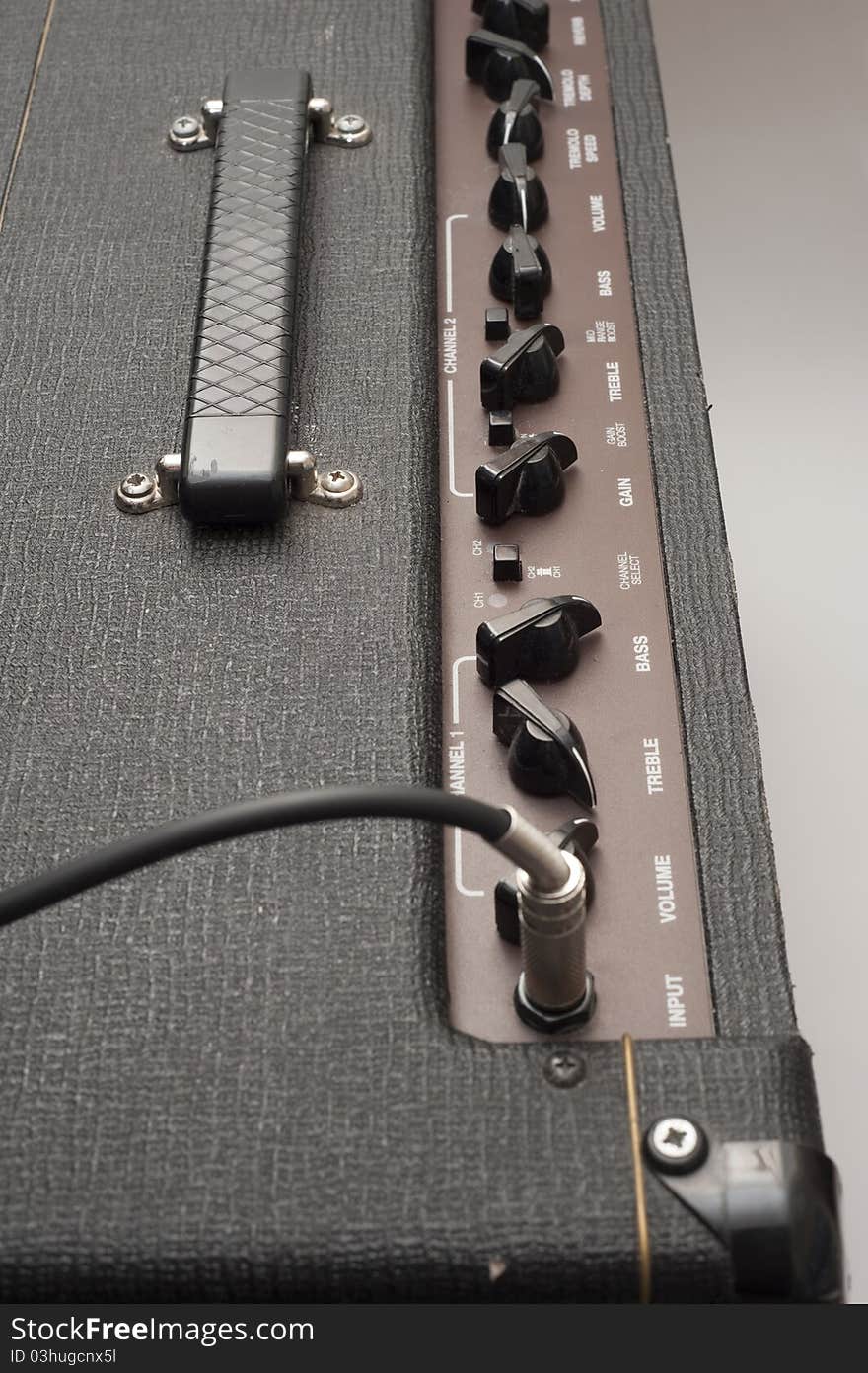 Close-up detail showing the chicken head knobs and controls of a classic British vintage valve guitar amplifier. The guitar jack input cable is visible in the foreground, as are various patches of superficial wear and tear damage to the tolex cover material on the amplifier. Close-up detail showing the chicken head knobs and controls of a classic British vintage valve guitar amplifier. The guitar jack input cable is visible in the foreground, as are various patches of superficial wear and tear damage to the tolex cover material on the amplifier.