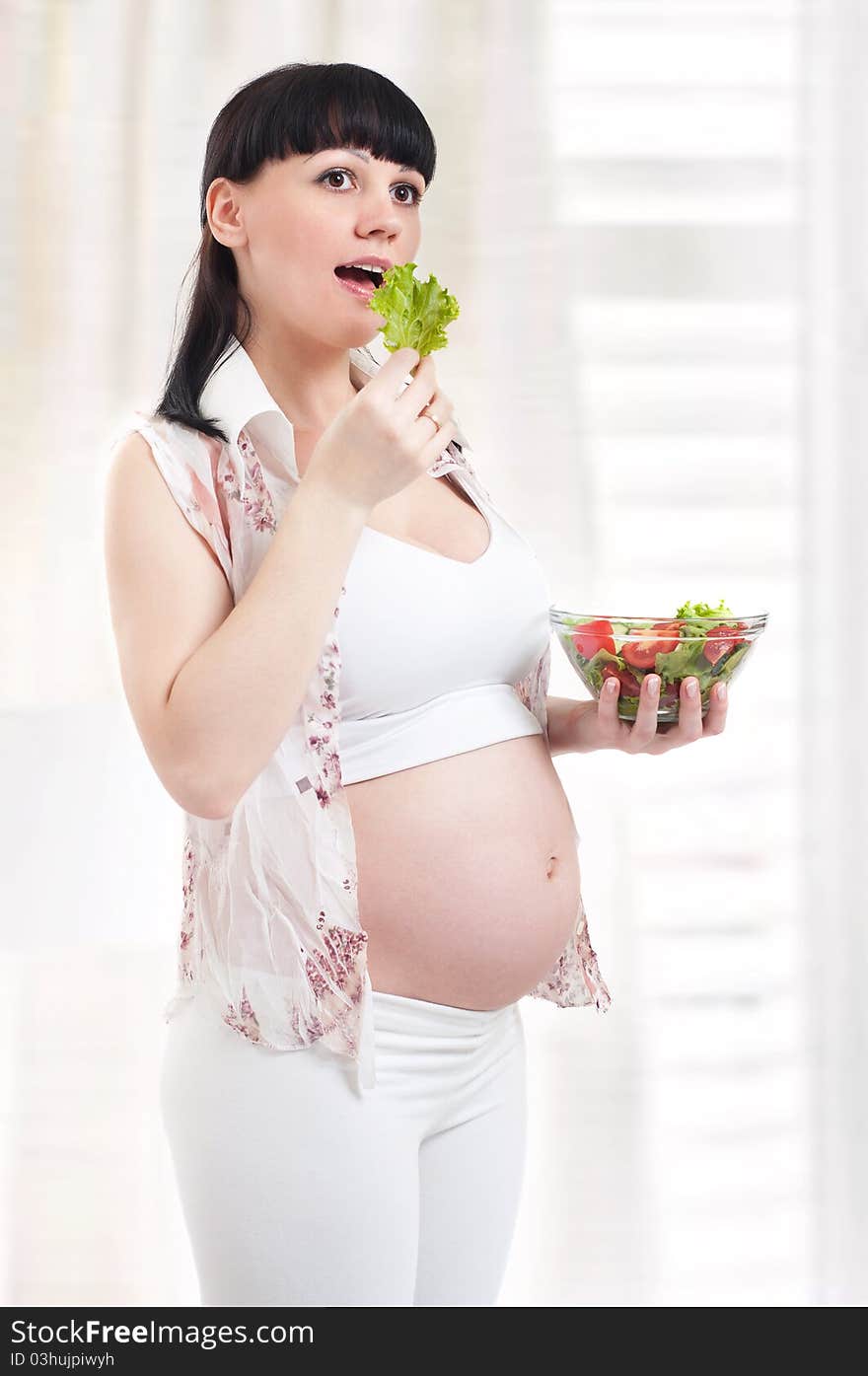 Pregnant woman with a plateful of salad in kitchen