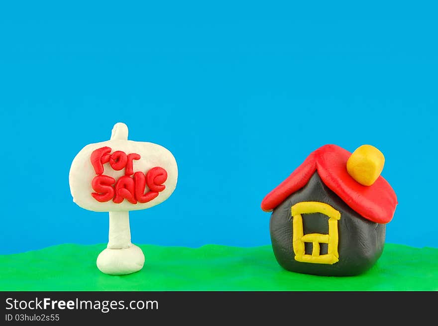 Plasticine house and For Sale real estate sign on plasticine grass and sky with place for your text. Plasticine house and For Sale real estate sign on plasticine grass and sky with place for your text