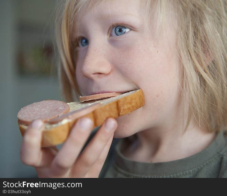 Young blond boy eating sandwich with salami